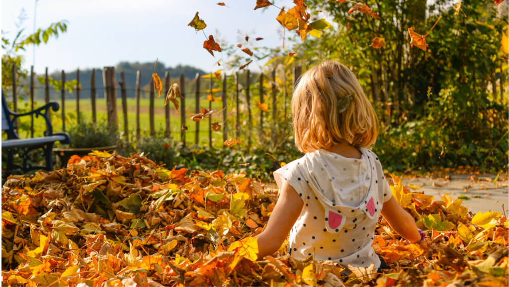 Blond girl with a hoodie in a pile of autumn leaves